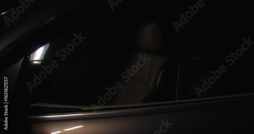 A car thief in black gloves pulls the car door handle at night, trying to rob or steal a car, and gets in.Concept for advertising the installation of alarm systems or guarded parking