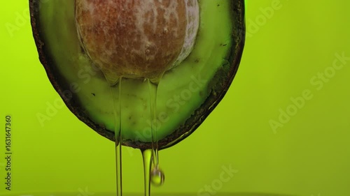A stream of oil flows from a beautiful ripe avocado fruit on a green background in slow motion 