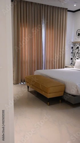 A smooth video reveal from wall to room with white bed, yellow bed bench, mirror on wall and soft curtains — cozy minimal bedroom interior in warm daylight.

