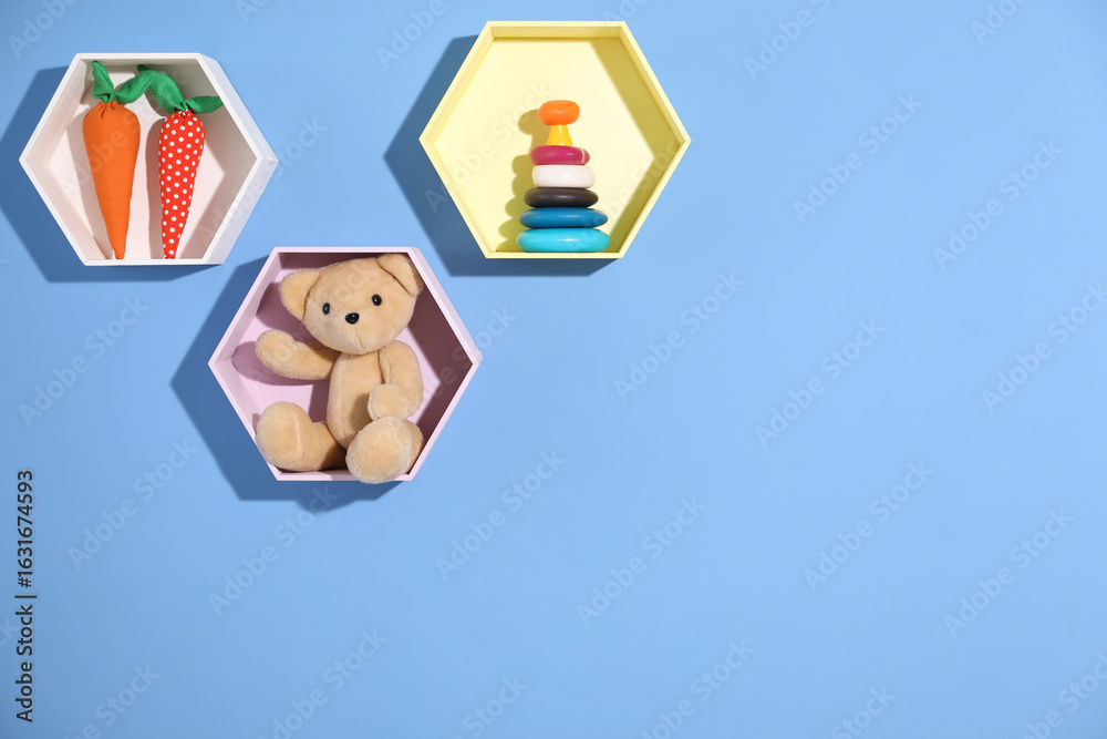 Obraz premium Honeycomb shaped shelves with different toys on blue background. Space for text