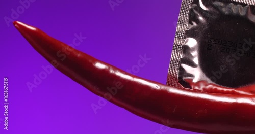 Extreme close-up  holding condom and a red chilli pepper  on a lilac background