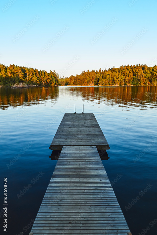 Obraz premium Holzsteg am See in Schweden – Abendstimmung mit Inseln, Wald und Spiegelungen
