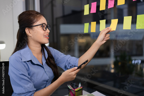 Asian businesswoman with paper notes creating project plan on office glass wall, Creative businesswoman, 