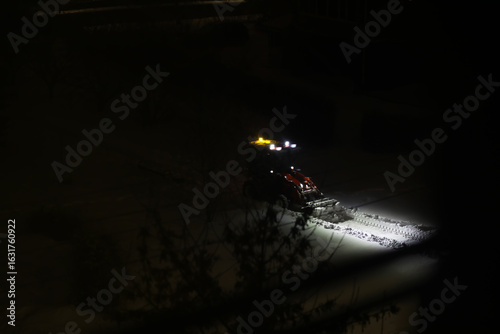 фотографія Snowplow Clearing Snow on a Dark, Snowy Night with Bright Lights Illuminating Pa