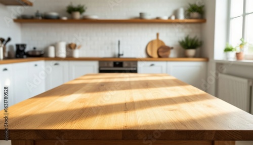 An empty wooden table with a bright white kitchen interior with a blurred background bathed in the early morning sun