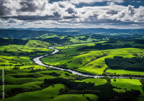 Serpentine river winding through lush green rolling hills under a dramatic cloudy sky