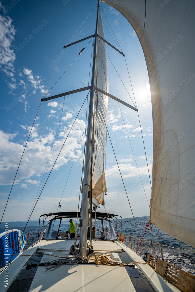 Fototapeta premium White sails filled with wind, seen from the bow of a sailing yacht near Croatia. Freedom, clean energy, adventure and mindful travel on the open sea.