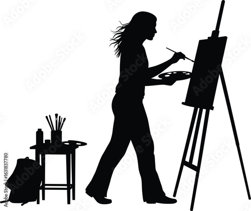 Silhouette of female artist painting on canvas with palette and brush beside art tools, table, backpack in creative studio
