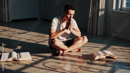 Man kneeling on carpet praying silently in soft light. Alone and meditating, man feels emotional calm. Sitting quietly, thinking man repeats praying gesture in peaceful spiritual mood