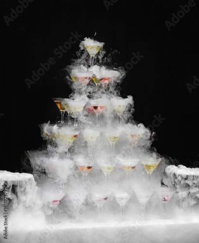 Ethereal mist envelops a whimsical tower of cocktail glasses, conjuring Gatsby-era glamour, perfect for Halloween or a steampunk celebration