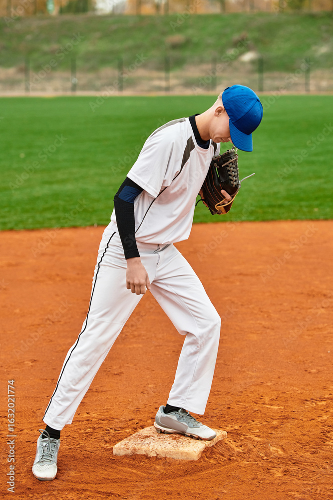 Skillful teenage boy prepares for a pitch on a bright baseball field at dusk Skillful teenage boy prepares for a pitch on a bright baseball field at dusk