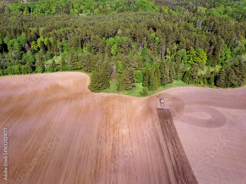 Aerial view landscape with plowed fields and tractor and forest on spring sunny day
