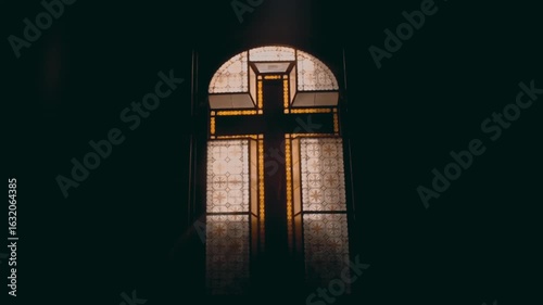 Golden stained glass cross window centered in dark cathedral interior with intimate close up view, representing Christian sacred architecture and spiritual heritage
