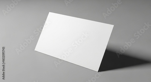 Clean white paper mock-up stands angled on a gray surface with a cast shadow, ideal for showcasing business cards, invitations, or graphic design layouts in minimalist style.