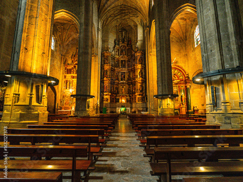 Interior of Iglesia de San Vicente in San Sebastian, Spain, with vaulted ceilings, stone columns, stained glass, wooden pews, and an ornate altarpiece.