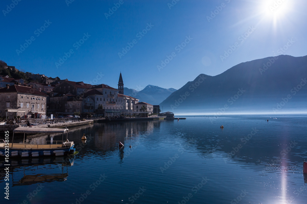 Fototapeta premium Distant view of the historic town of Perast, Montenegro, on a peaceful winter evening. The Adriatic coast with soft fading light creates a serene Mediterranean atmosphere.