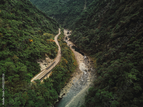 Aerial view of a winding road through a lush, mountainous valley with a river running through it.
