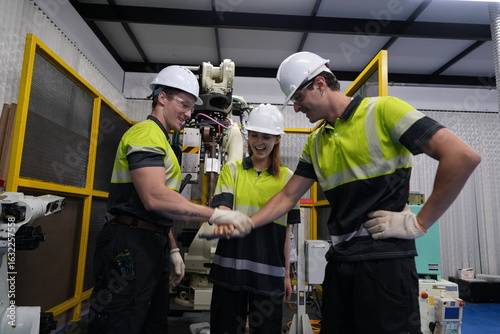 team of male and female engineers join hands and happily repair a remote control circuit board to set the working command of a robot arm in a factory to determine the production line in the factory.