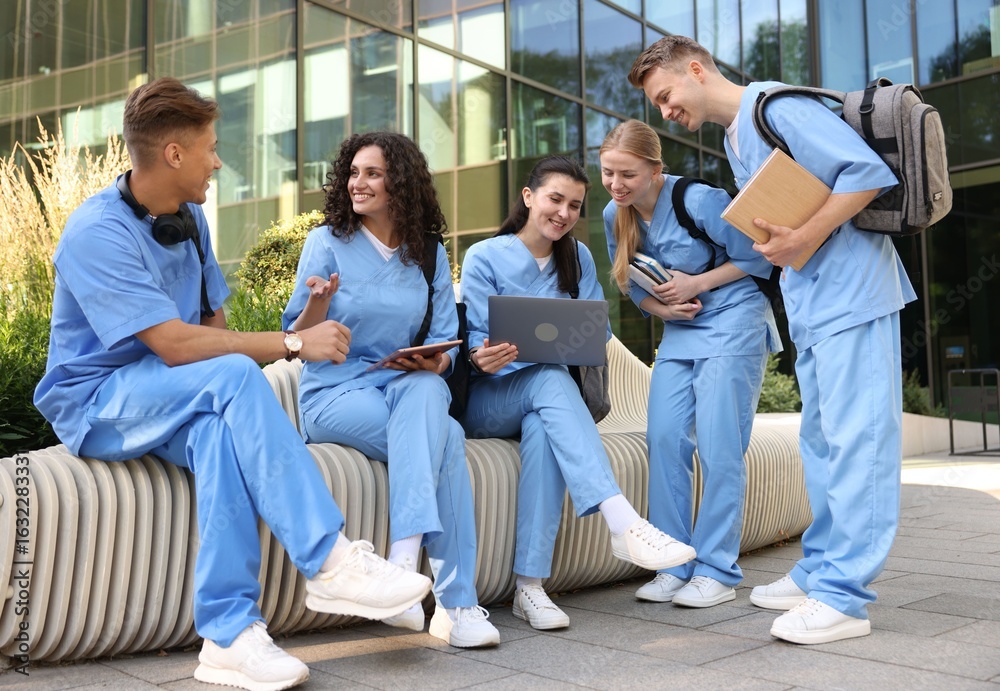Fototapeta premium Group of medical students in uniforms studying together near building outdoors