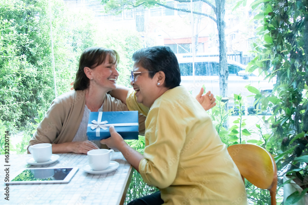 Obraz premium Two senior women friends embrace warmly while exchanging a gift at the cafe. retired people bonding relationship impression showing lasting friendship celebration of special birthday happiness moment