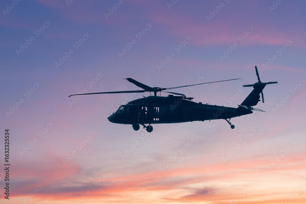 Fototapeta premium A silhouette of a military helicopter flying against a bright blue sky, showcasing its structure and movement during an airborne operation.
