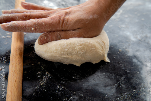 Close-up of a hand kneading fresh dough on a floured countertop. Homemade baking process captured in a warm and rustic kitchen environment. 