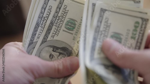 Hands counting 100-dollar bills over a table. Close-ups and different angles of cash handling, showing fingers flipping, stacking, and spreading US dollars.