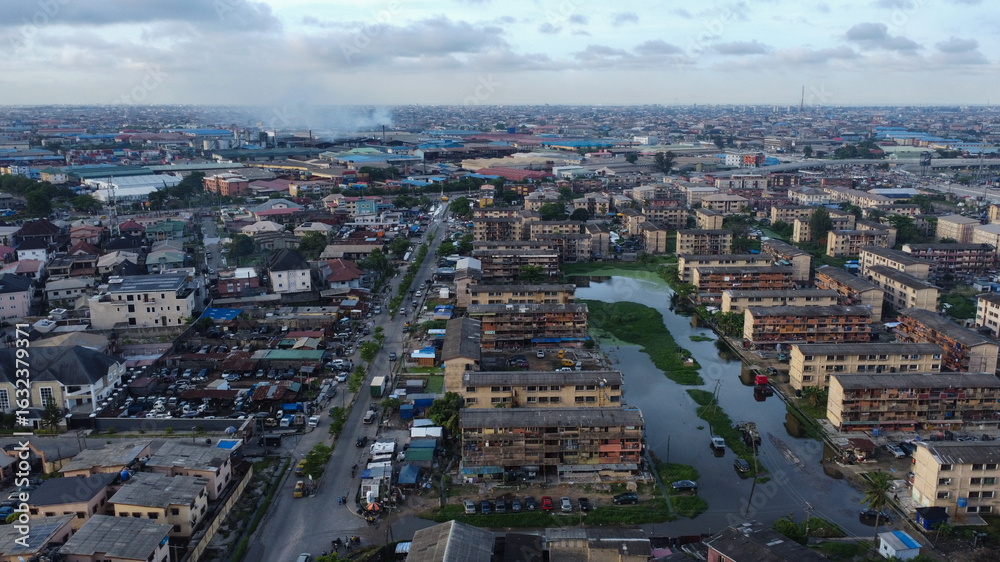 Obraz premium Expansive aerial view of Lagos, Nigeria showcases dense urban landscape under a cloudy sky.