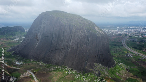 Aerial View of Zuma Rock: Nigeria's Iconic Monolith Dominates a Lush Landscape with Distant City