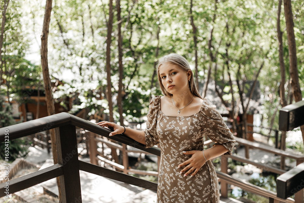 Naklejka premium Girl in floral dress leaning on metal railing