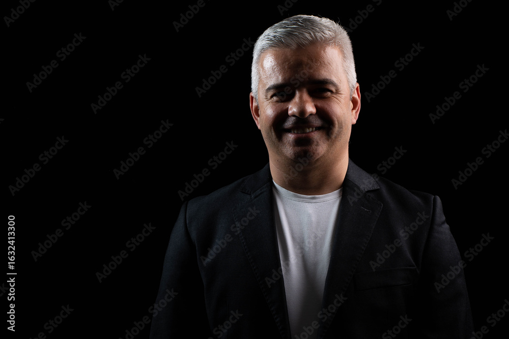 Fototapeta premium Smiling businessman standing confidently under chiaroscuro lighting, professional studio portrait on dark background