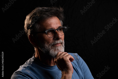 Obraz na płótnie Mature man posing under chiaroscuro light with positive yet mysterious gaze, dra