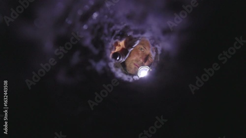 Man inspecting a dryer vent with a flashlight, checking for lint buildup and blockages. The image captures a real-life home maintenance moment, emphasizing fire prevention, appliance safety, and respo