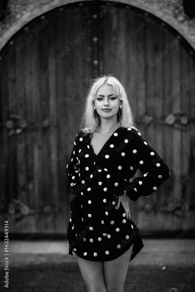 Naklejka premium Portrait of a beautiful blonde girl in a white polka dot dress outdoors. Black and white photo.