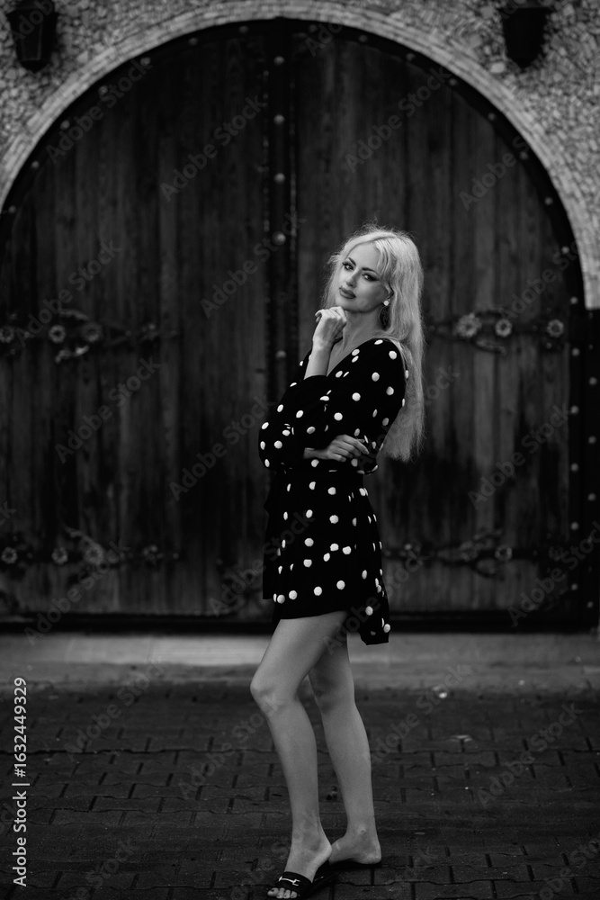 Naklejka premium Portrait of a beautiful blonde girl in a white polka dot dress outdoors. Black and white photo.