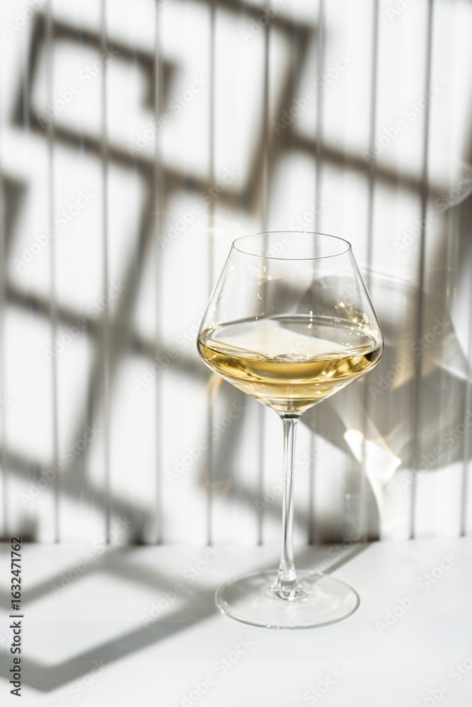 Obraz premium A glass of white wine on the white background with geometric shadow effect, modern composition.