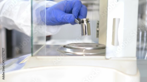 A operator's hand is holding steel calibration weight to place on the analytical balance.