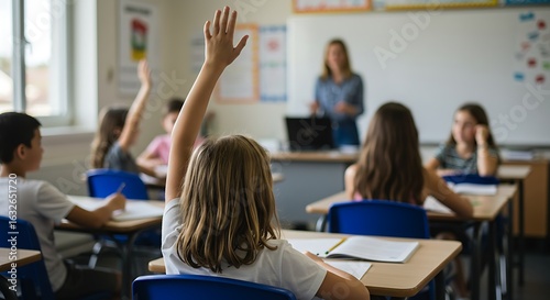 Young student raising hand in a bright elementary school classroom with a teacher.