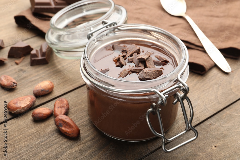 Fototapeta premium Delicious chocolate panna cotta in glass jar, nuts and spoon on wooden table, closeup