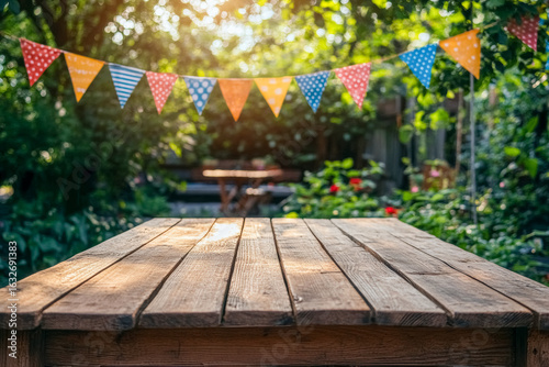 Empty wooden table and colorful festive flags adorn vibrant outdoor backyard garden setting for celebration, party or picnic, blurred background for product or montage