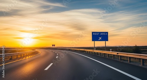 Asphalted Highway Leads To Horizon At Sunset With Rest Area Sign