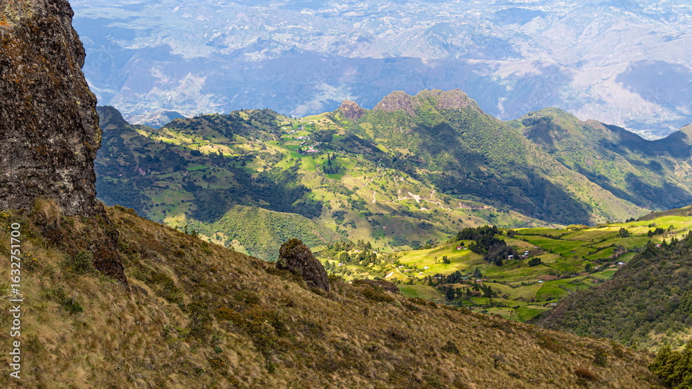 Fototapeta premium Panoramic view of a mountain range, valley and small village from the top of the Bolarrumi Rock Complex located on highlands of the Huasipamba community, canton Santa Isabel, Azuay, Ecuadorian Andes