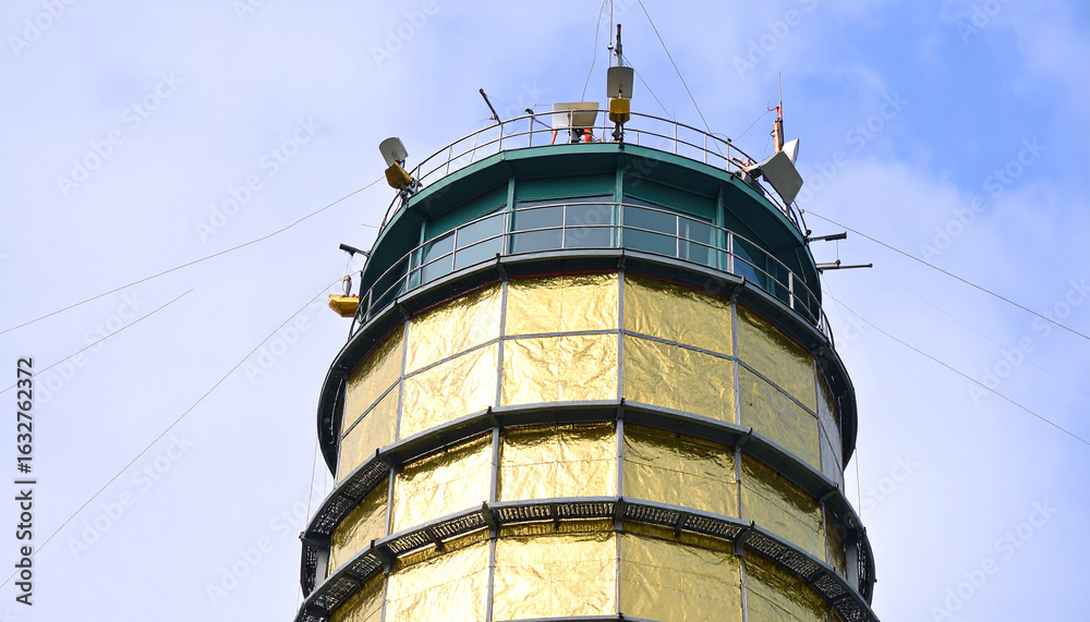 Naklejka premium Golden Tower Ascending: An imposing tower of shining gold rises against a bright sky, its architecture echoing both classic design and modern purpose. The pinnacle of ingenuity.