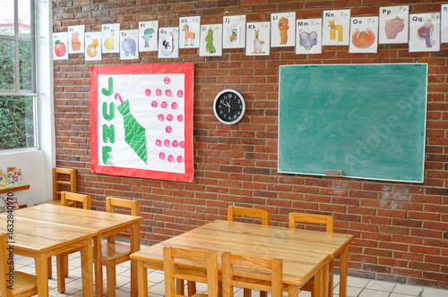 Preschool classroom with wooden desks, chalkboard, and alphabet posters