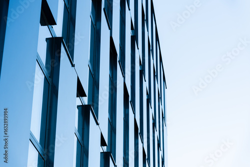 Contemporary office building facade with reflective glass windows and geometric lines, captured in a minimalist architectural style. Suitable for illustrating business, corporate, architecture, or