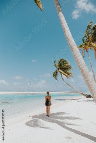 Woman standing on pristine beach under palm trees on Tikehau Island, French Polynesia.
