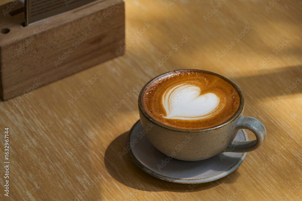 Obraz premium latte coffee art on wooden plate at desk in sun shine with shade of the tree