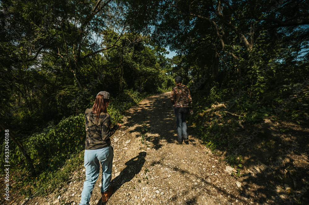 Naklejka premium Mother and daughter dressed in hiking clothes, walking along a trail in the middle of the rainforest.