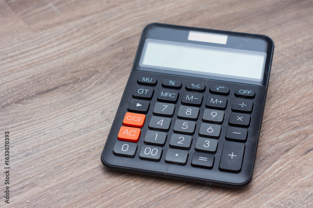 Modern black digital calculator with LCD display on a natural wooden desk surface. Professional office equipment for business calculations, accounting, and financial planning tasks. Modern black digital calculator with LCD display on a natural wooden desk surface. Professional office equipment for business calculations, accounting, and financial planning tasks.