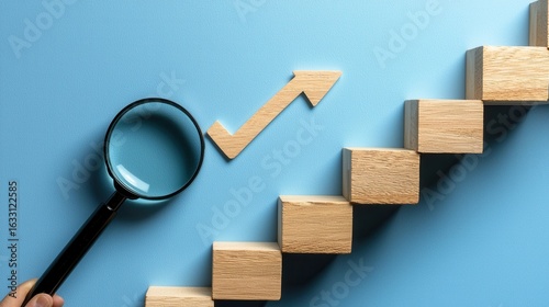A close-up of a hand holding a magnifying glass, focusing on a wooden staircase symbolizing growth, against a serene blue background. Perfect for business or educational themes.